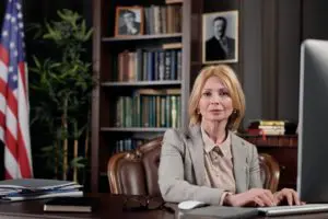 Professional woman sitting at desk with bookshelves behind.
