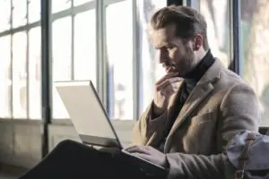 Man in a suit working on a laptop by a window.