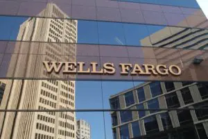 Wells Fargo sign reflected on a glass building with city skyscrapers.
