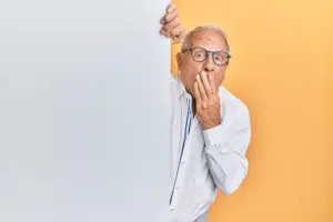 Elderly man with glasses expressing surprise against a split grey and orange background.