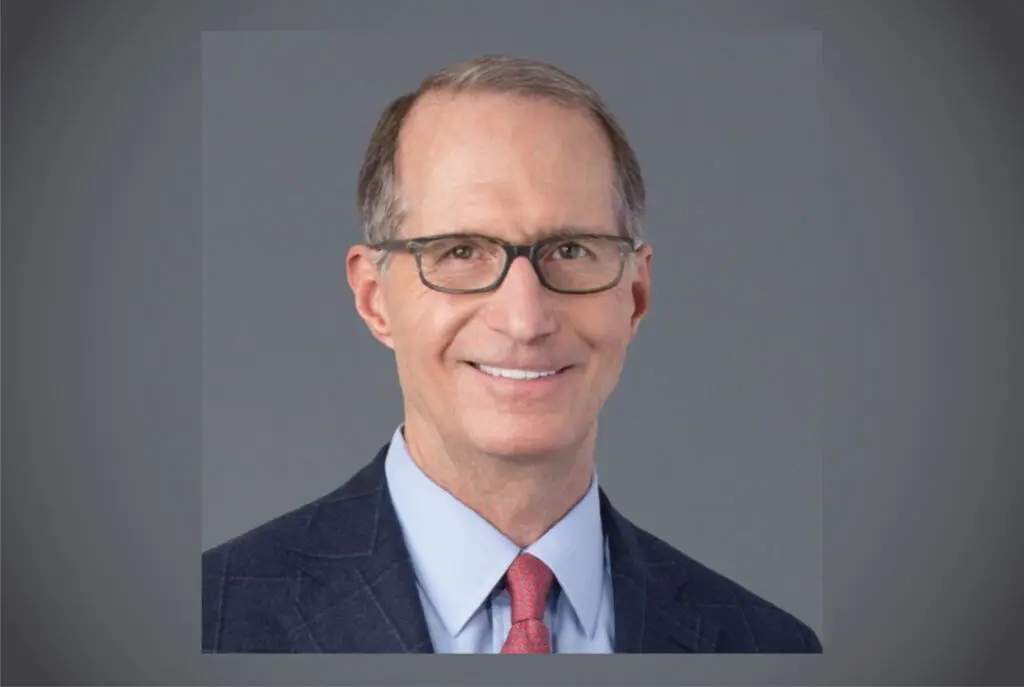 Professional headshot of a middle-aged man wearing glasses and a suit.