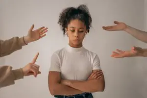 A young woman looks upset while several hands point at her.